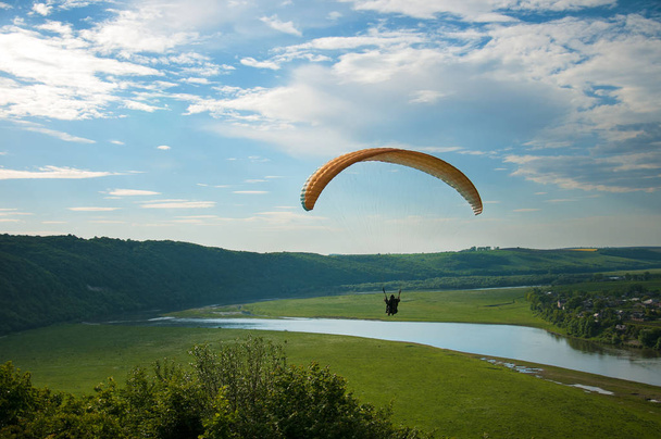 Αλεξίπτωτο πλαγιάς πάνω από το πράσινο πεδίο στην ηλιόλουστη μέρα του καλοκαιριού. Ένα αλεξίπτωτο που πετούν πάνω από το πράσινο πεδίο κοντά στον ποταμό Dnister στην Ουκρανία. - Φωτογραφία, εικόνα