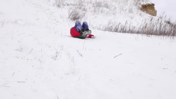 vidám gyermek a piros kabát diák szán a hóban egy magas hegy és nevet. boldog lány játék karácsonyi ünnep a téli park. Lassú mozgás - Felvétel, videó