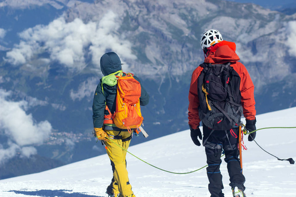Alpinistas amarrados escalando montanha com campo de neve amarrado com uma corda com machados de gelo e capacetes
. - Foto, Imagem