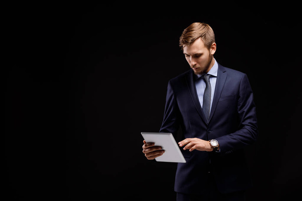 Portrait of a young successful businessman with the tablet computer on a black background. A happy leader in an elegance suit. - Фото, зображення
