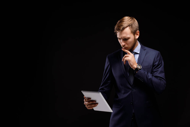 Retrato de un joven empresario exitoso con la tableta sobre un fondo negro. Concepto tecnológico
 - Foto, Imagen