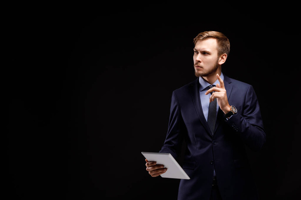 Portrait of a young successful businessman with the tablet computer on a black background. Technology concept - Фото, зображення