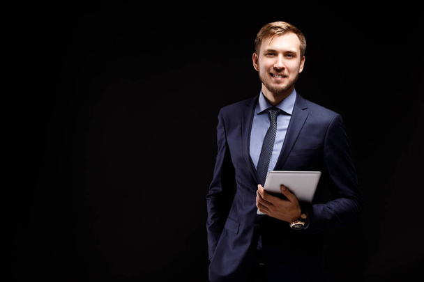 Portrait d'un jeune homme d'affaires prospère avec la tablette sur fond noir. Un leader dans un costume d'élégance
. - Photo, image