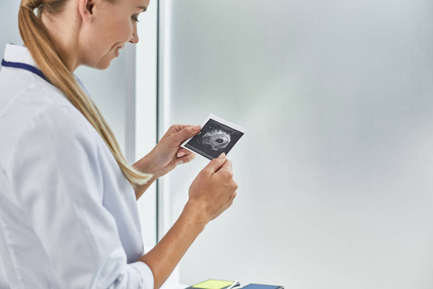Young doctor looking at ultrasound picture of future baby - Photo, image