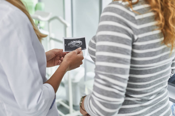 Lääkäri seisoo tulevan äidin vieressä ja pitää ultraäänikuvan
 - Valokuva, kuva