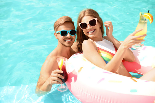 Young couple with cocktails in pool on sunny day - Photo, Image