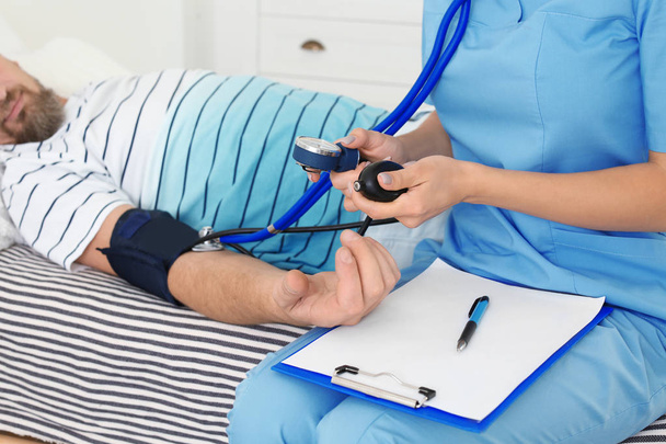 Assistente medico femminile che misura la pressione sanguigna del paziente maschile durante la visita a casa
 - Foto, immagini