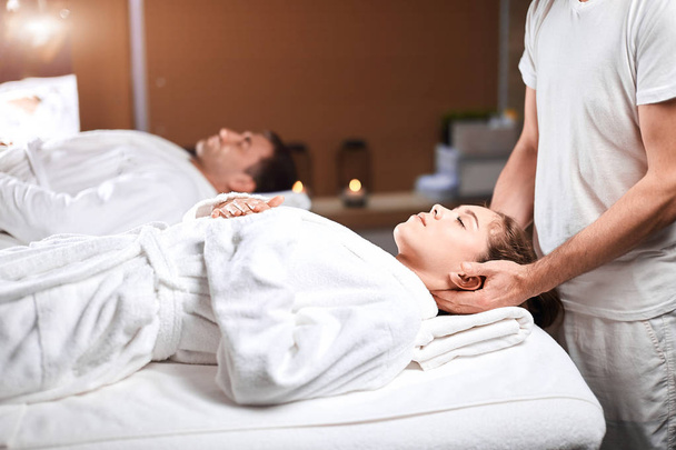 Mooie jonge vrouw ontvangt massage op hoofd en schouders zone in spa centrum - Foto, afbeelding