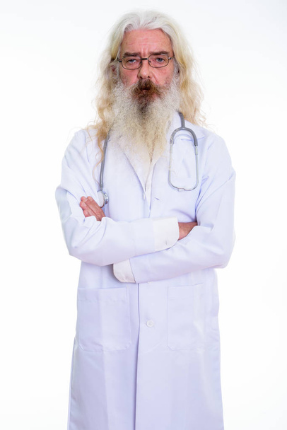 Studio shot of senior bearded man doctor standing while wearing  - Foto, Bild
