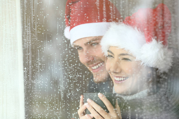 Happy couple looking through a window at home or hotel in christmas - Photo, Image