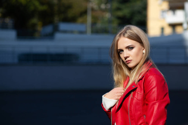 Fashionable blonde woman with long hair wearing leather jacket posing with sun light. Space for text - Foto, immagini