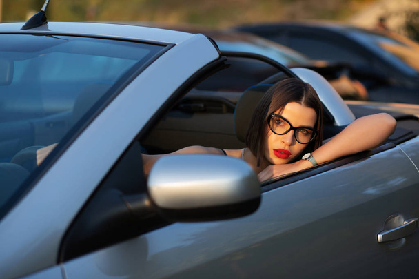 Nahaufnahme Porträt einer attraktiven jungen Frau mit roten Lippen, die im Cabriolet posiert. Raum für Text - Foto, Bild