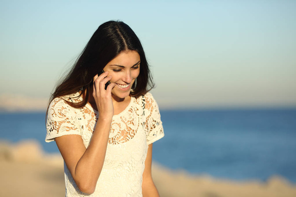 Mujer feliz hablando por teléfono caminando en la playa en un día soleado
 - Foto, Imagen