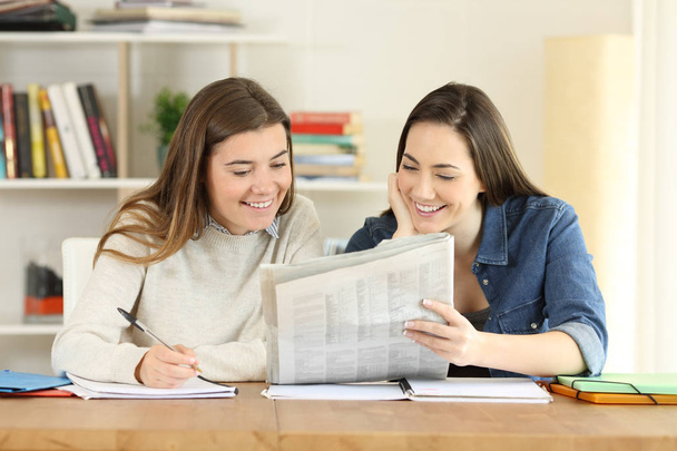 Two happy students talking about newspaper news at home - Foto, afbeelding