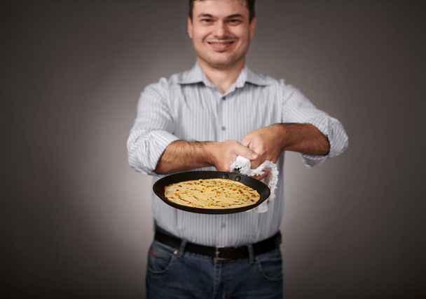 uomo in posa con un pancake in una padella, camicia bianca e pantaloni, sfondo grigio, profondità di campo poco profonda, frittella affilata e viso sfocato
 - Foto, immagini
