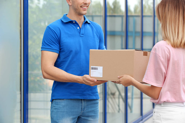 Young woman receiving parcel from courier outdoors. Delivery service - Foto, Imagen