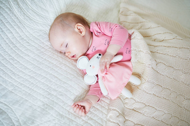 Baby girl having a nap with her favorite mouse toy. Little child sleeping on bed with comforter. Infant kid in sunny nursery - Foto, Imagem
