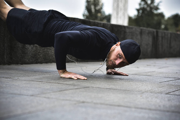 Молодой бородатый спортсмен делает тренировку в парке, делая серию отжиманий на открытом воздухе
. - Фото, изображение
