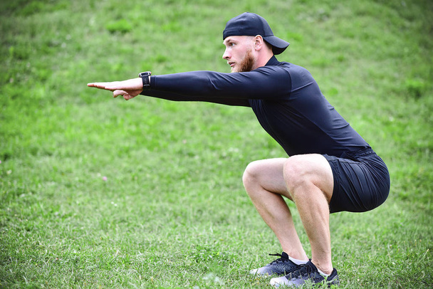 Full length of young concentrated sportsman doing squats outdoors. - Photo, Image