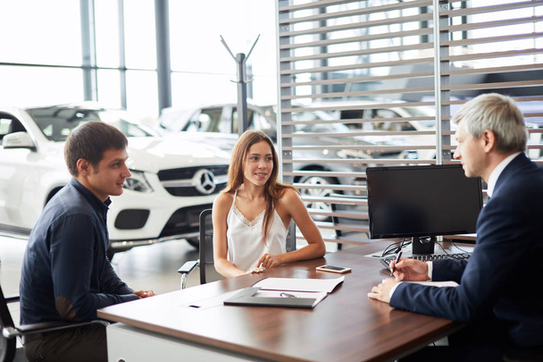 Mature sales manager signing contract with clients at car dealership office - Фото, зображення