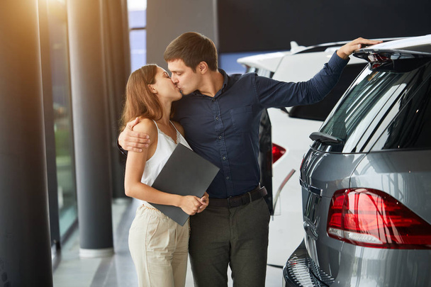 Young car salesman telling about features of car to female customer - Foto, afbeelding