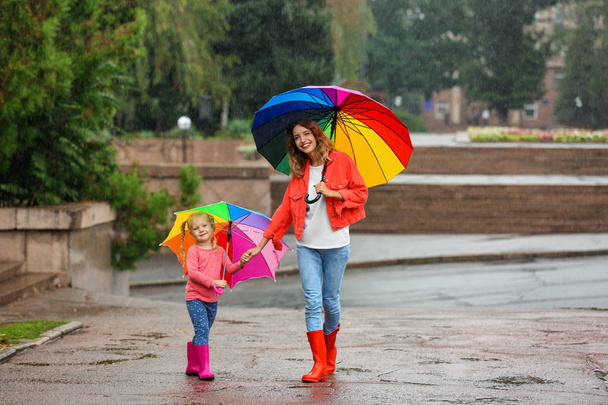 Happy mother and daughter with bright umbrella under rain outdoors - Foto, Imagen