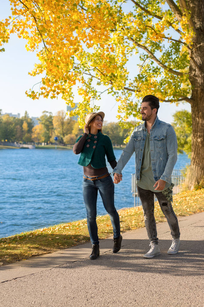 Pareja feliz caminando en un parque junto al agua en otoño durante el día
 - Foto, Imagen