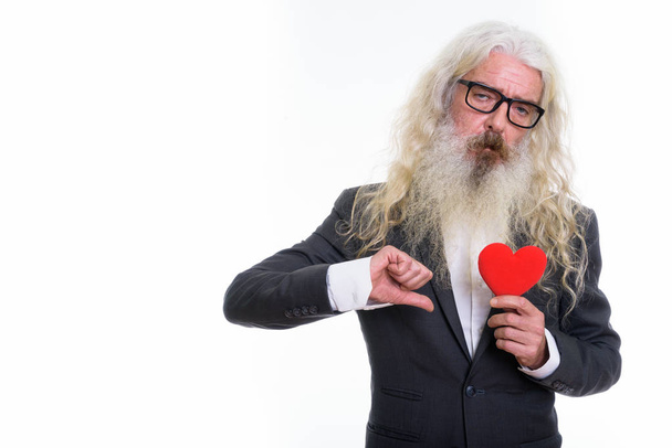 Studio shot of senior bearded businessman holding red heart and  - Foto, afbeelding