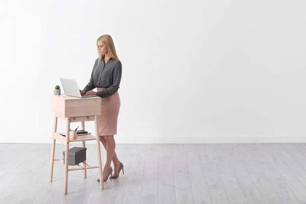 Young woman using laptop at stand up workplace against white wall. Space for text - Foto, Bild