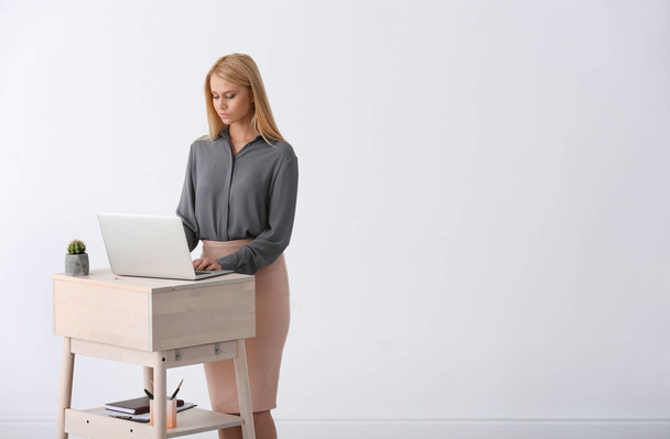 Young woman using laptop at stand up workplace against white wall. Space for text - Foto, Imagem