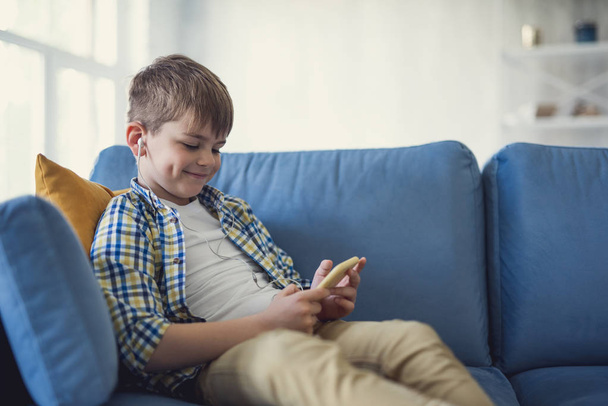 Szczęśliwy chłopiec uśmiecha się i relaks z jego smartphone w domu - Zdjęcie, obraz