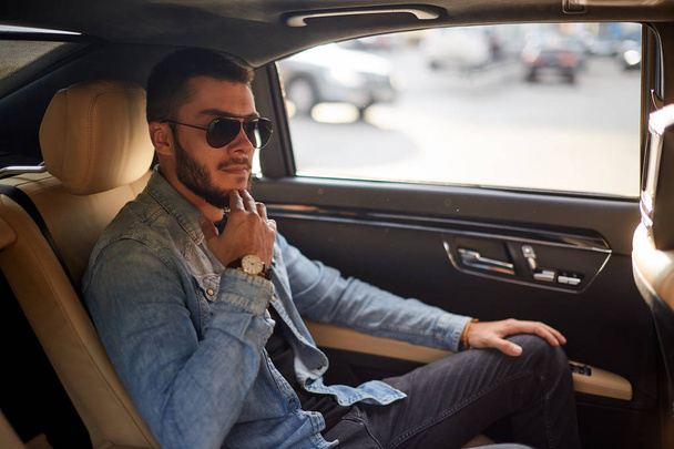 awesome businessman holding his chin while sitting on the back seat of a car - Foto, imagen