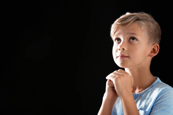 Little boy with hands clasped together for prayer on black background. Space for text - 写真・画像