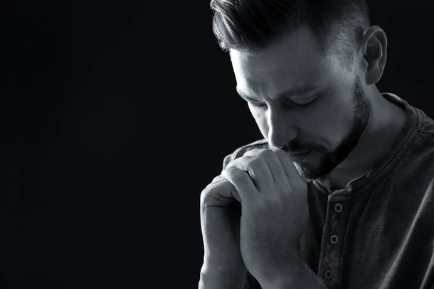 Man with hands clasped together for prayer on dark background, black and white effect. Space for text - Photo, image