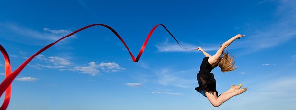 jymnast με κόκκινη κορδέλα άλμα κατά μπλε ουρανό - Φωτογραφία, εικόνα