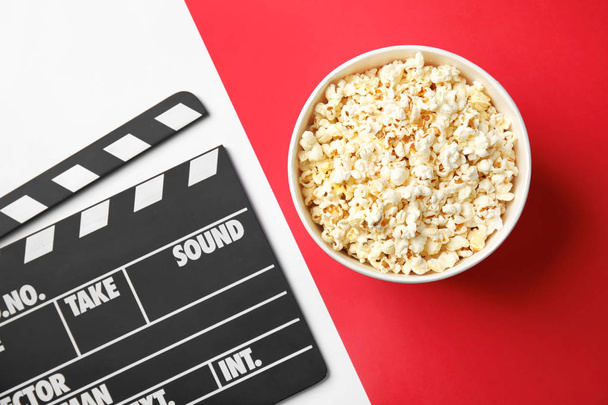 Tasty popcorn in paper cup and clapperboard on color background, top view. Cinema snack - Foto, immagini