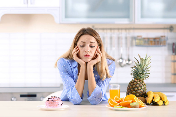 Woman choosing between dessert and fruits at table in kitchen. Healthy diet - Foto, Imagen
