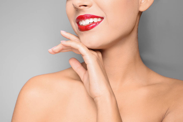 Beautiful young woman with red glossy lips on gray background, closeup - Valokuva, kuva