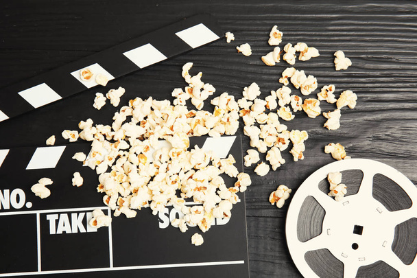 Tasty popcorn, film reel and clapperboard on wooden background, top view. Cinema snack - Фото, изображение