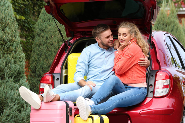 Happy young couple sitting in car trunk and suitcases outdoors - Foto, afbeelding