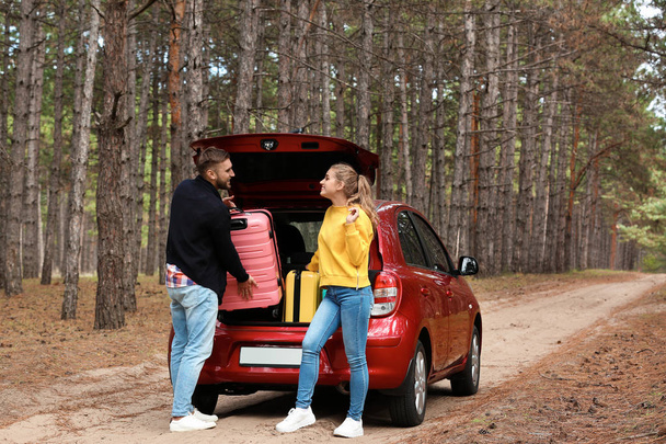 Young couple loading suitcases into car trunk on forest road - 写真・画像