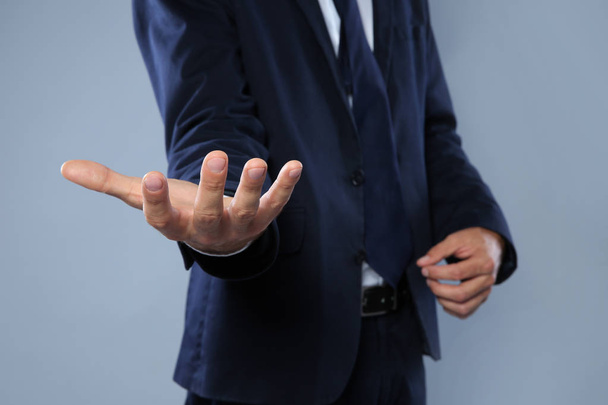 Businessman holding something on grey background, closeup of hands - Foto, immagini