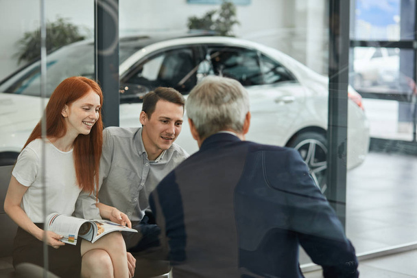 Happy beautiful couple is buying a new car at dealership. Family council - Foto, afbeelding