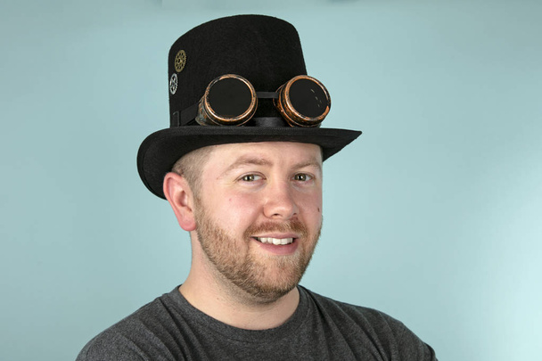Σοβαρές νεαρός γενειοφόρος άνδρας σε ένα κορυφαίο καπέλο πανηγυρικά κοιτάζοντας την κάμερα πάνω σε φόντο γκρι στούντιο - Φωτογραφία, εικόνα