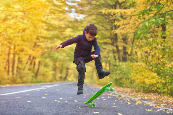 Kid skateboarder doing skateboard tricks in autumn environment - Fotó, kép