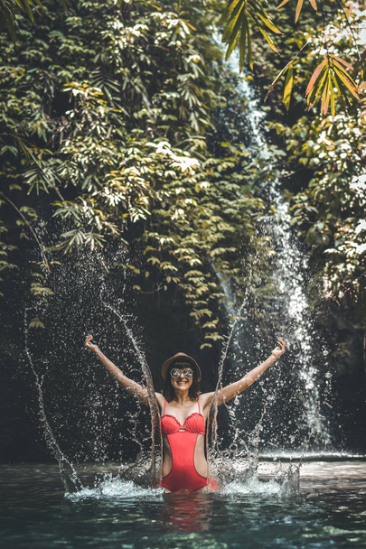 Gelukkig jonge vrouw toeristische met stro hoed in de diepe jungle met waterval. Echte avontuur concept. Bali eiland. - Foto, afbeelding