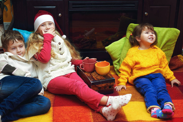 Vidám gyermekek meleg pulóverek, a kandalló mellett. A ház télen portré - Fotó, kép