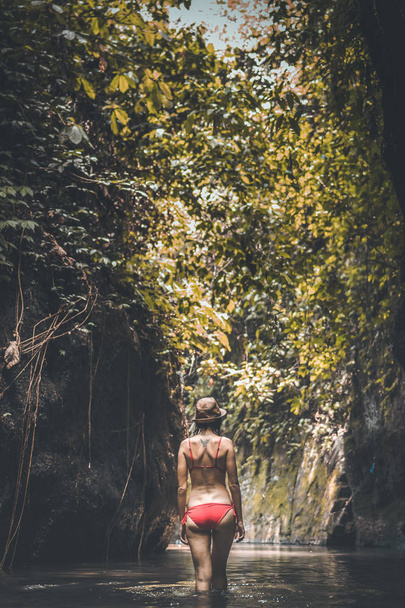 麦わら帽子と深いジャングルの中で赤い水着の若い女性観光客のリアビュー。本当の冒険のコンセプトです。バリ島. - 写真・画像