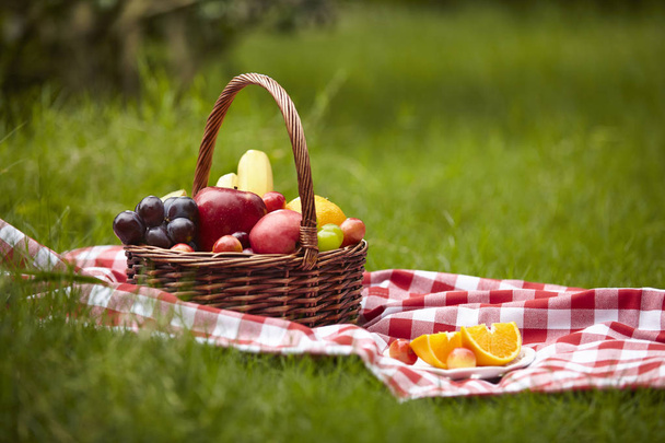 assorted fruits in a basket for picnic on grass. - Foto, imagen
