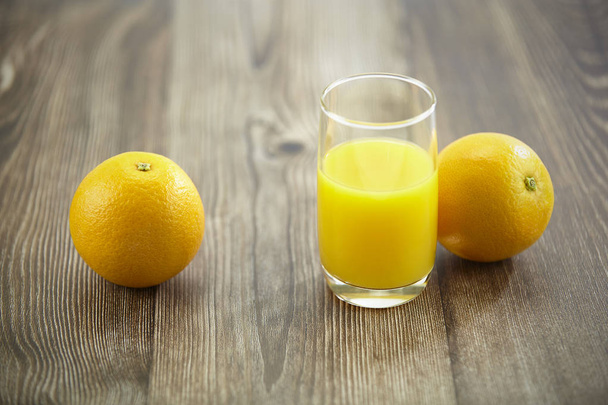два апельсина и стакан апельсинового сока на поверхности твердой древесины
. - Фото, изображение